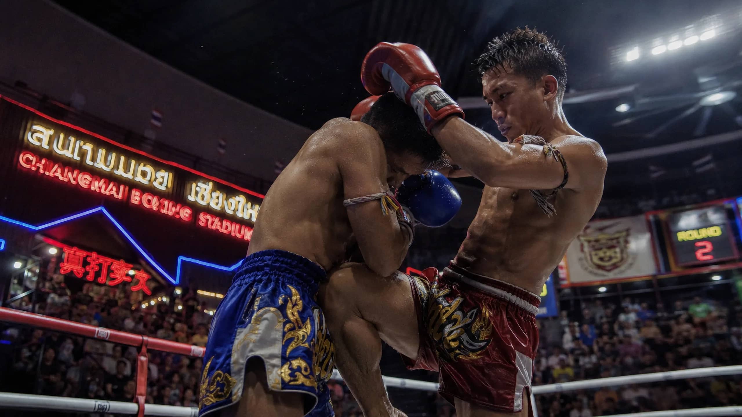 Two fighters grapple in a clinch with the stadium's neon sign glowing behind them