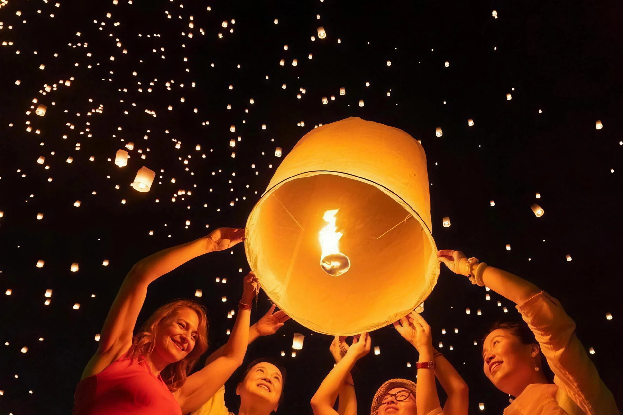 Smiling guests release a glowing paper lantern into a night sky filled with floating lanterns