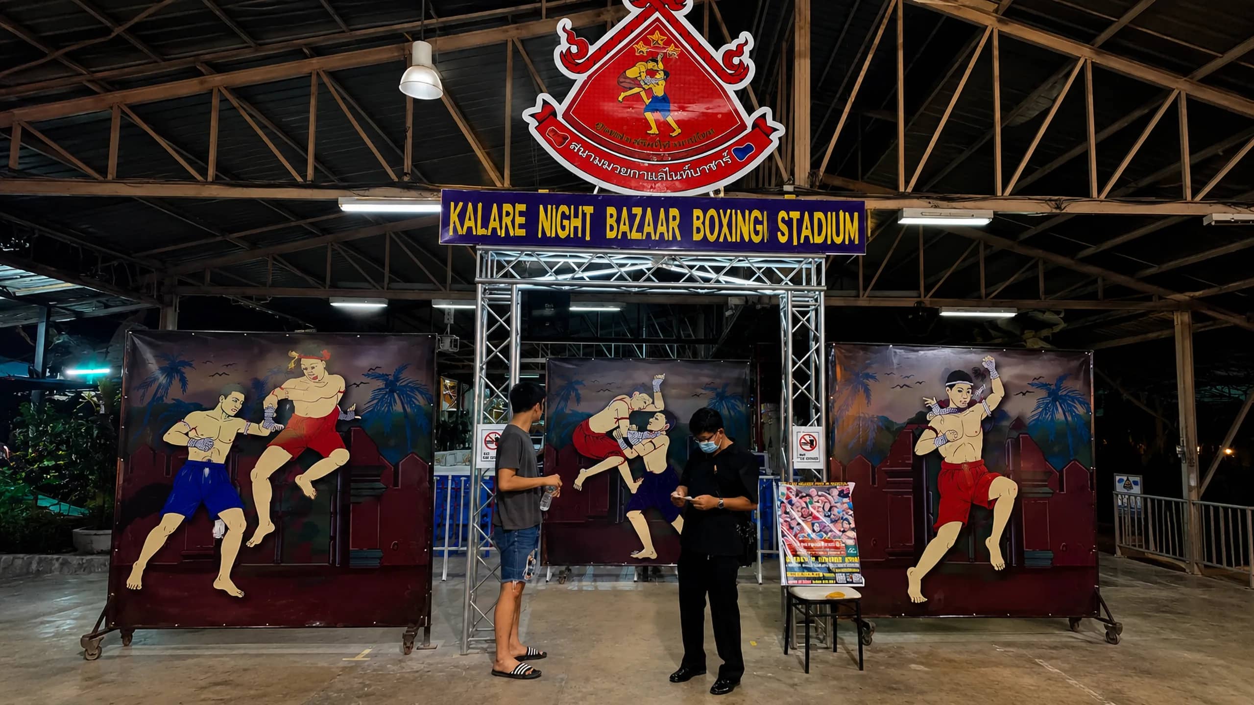 The entrance gate of the Night Bazaar boxing stadium with painted Muay Thai fighter murals at night