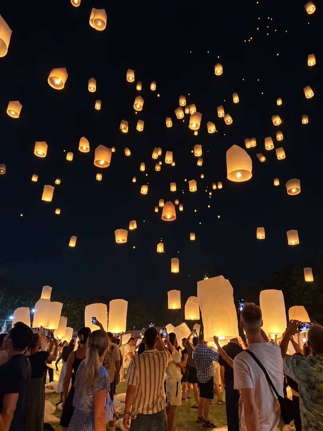 Hundreds of glowing sky lanterns rise into the dark sky above a crowd of festival guests
