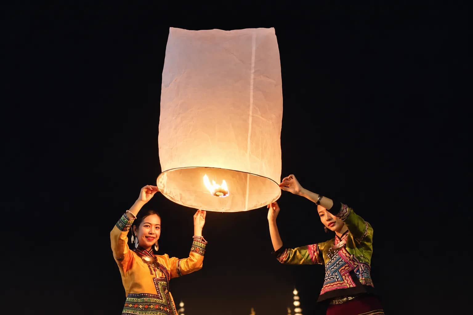Two women in traditional hill tribe dress hold a lit paper lantern ready for release