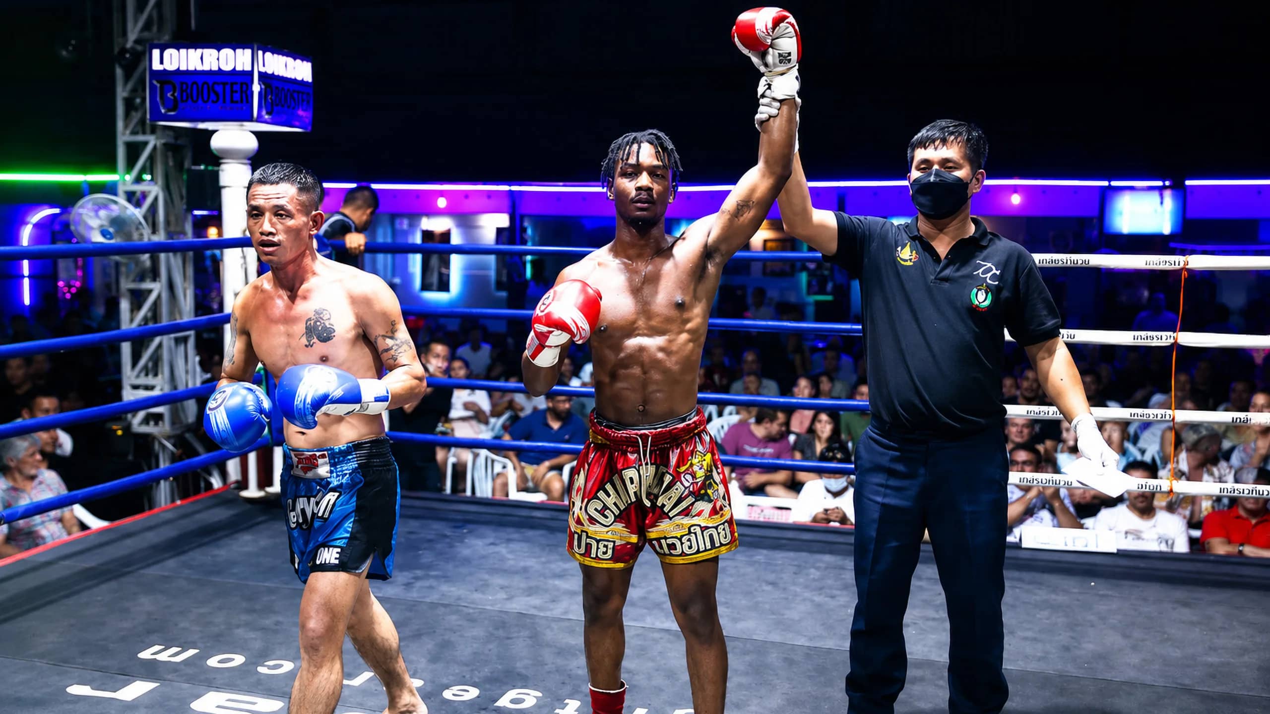 A referee raises the arm of the winning fighter after a Muay Thai bout at Loi Kroh Boxing Stadium