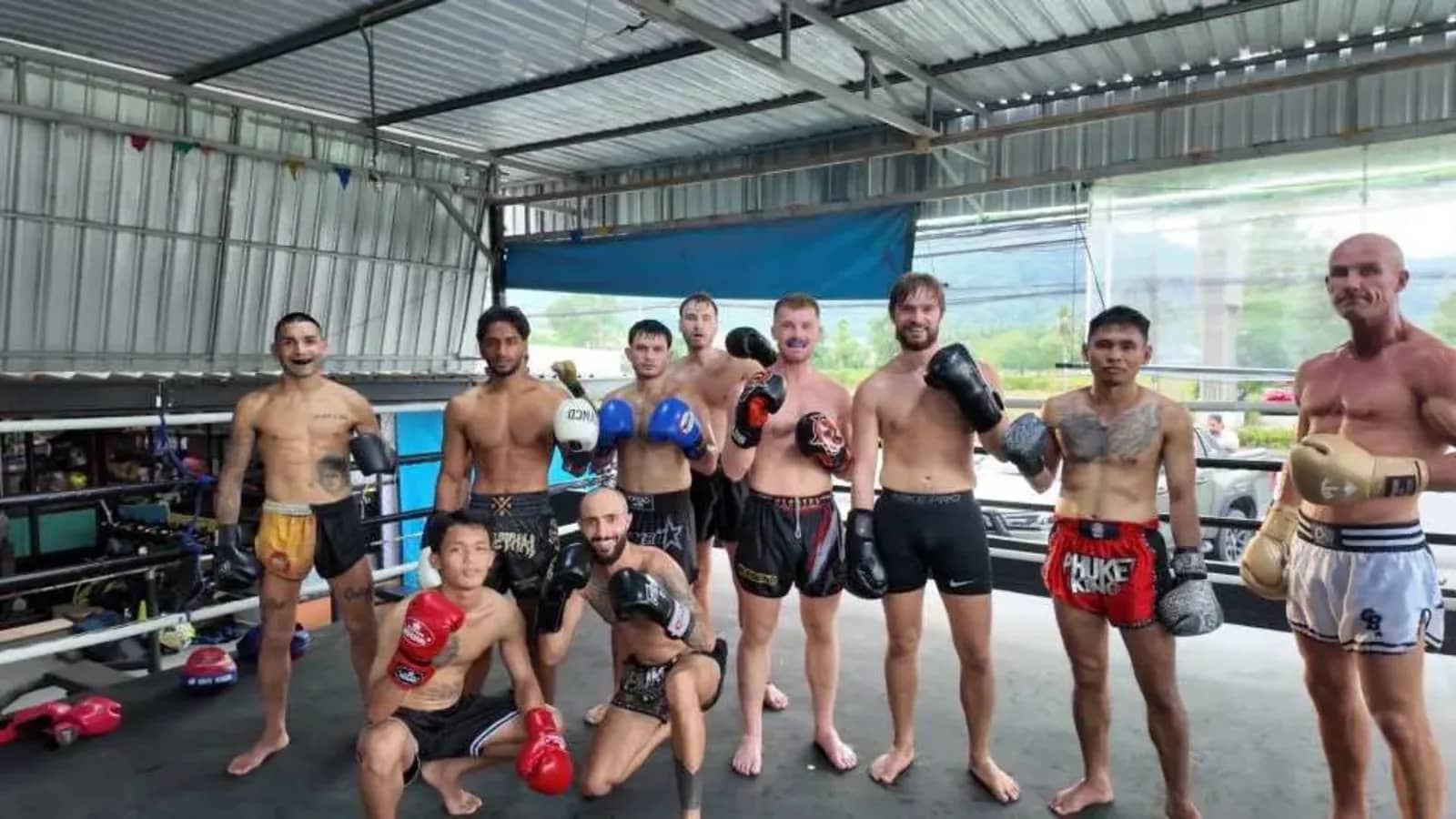 Muay Thai students and trainers in gloves and shorts pose in front of a boxing ring in Phuket
