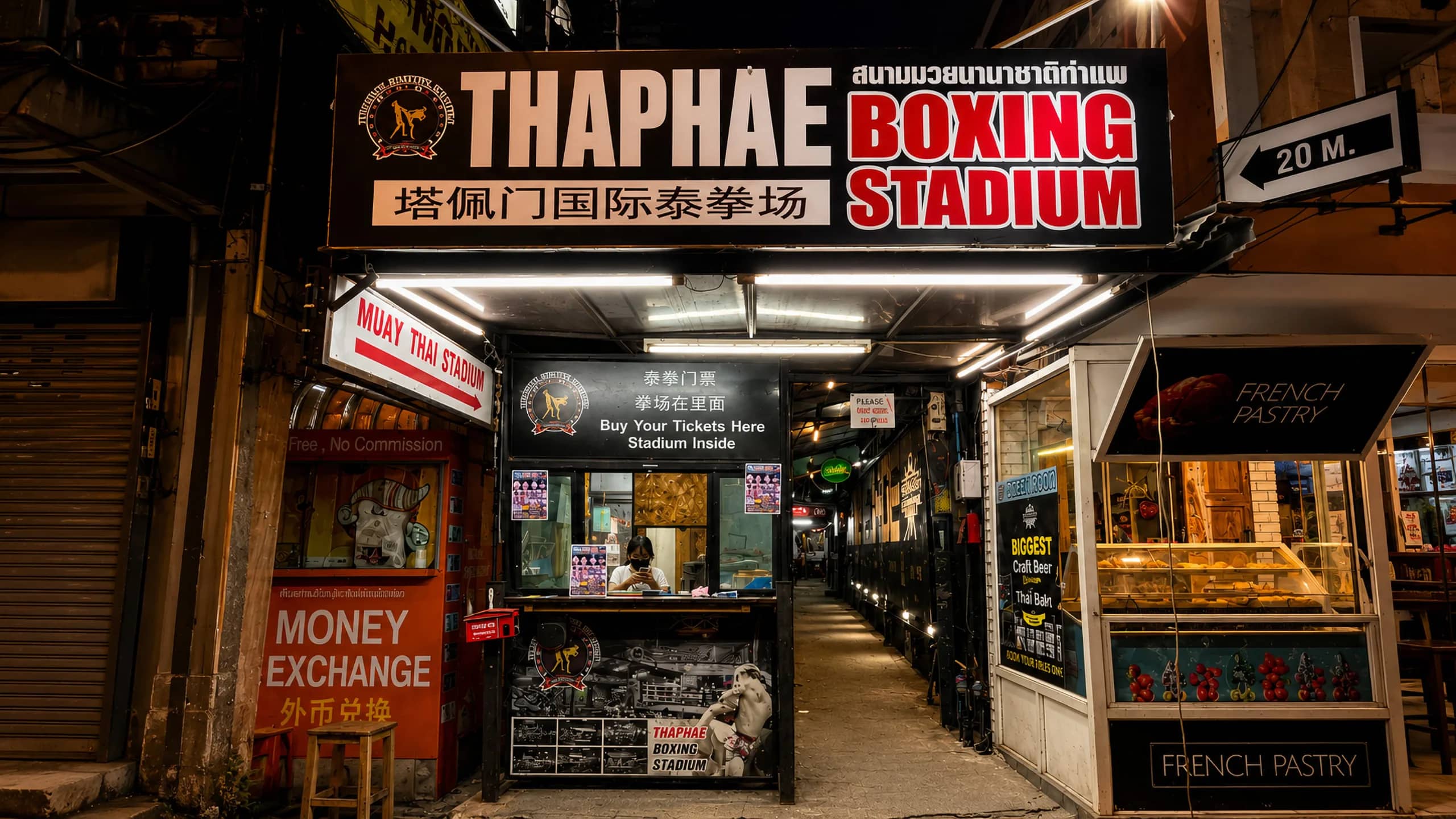 A narrow alley with a ticket booth leads into Thaphae Boxing Stadium beneath its bright sign