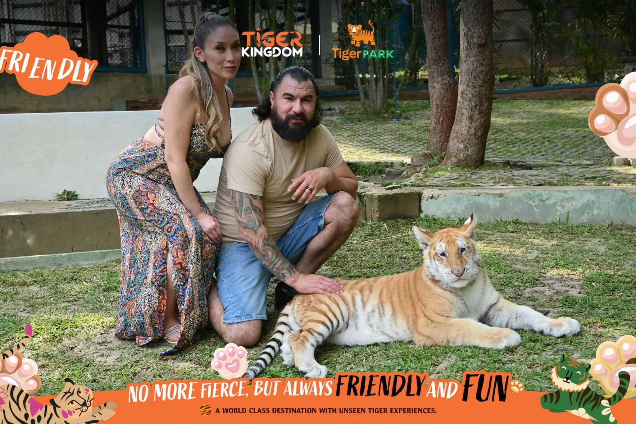 A couple crouches on the grass beside a young golden tiger inside a printed souvenir photo frame.