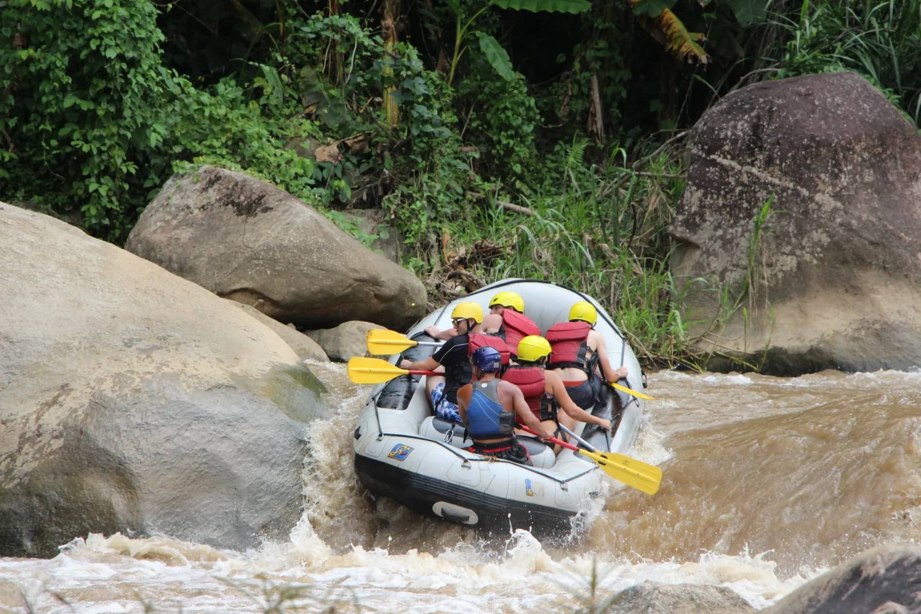 A raft full of paddlers in yellow helmets drops through a rapid between large boulders