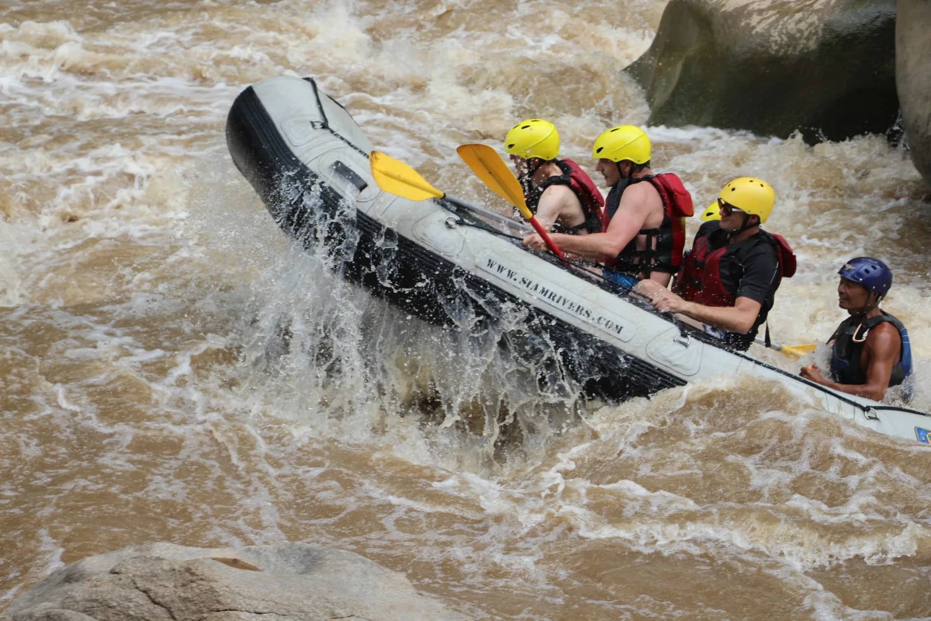 A raft tilts sharply as its crew in yellow helmets paddles through a steep white rapid