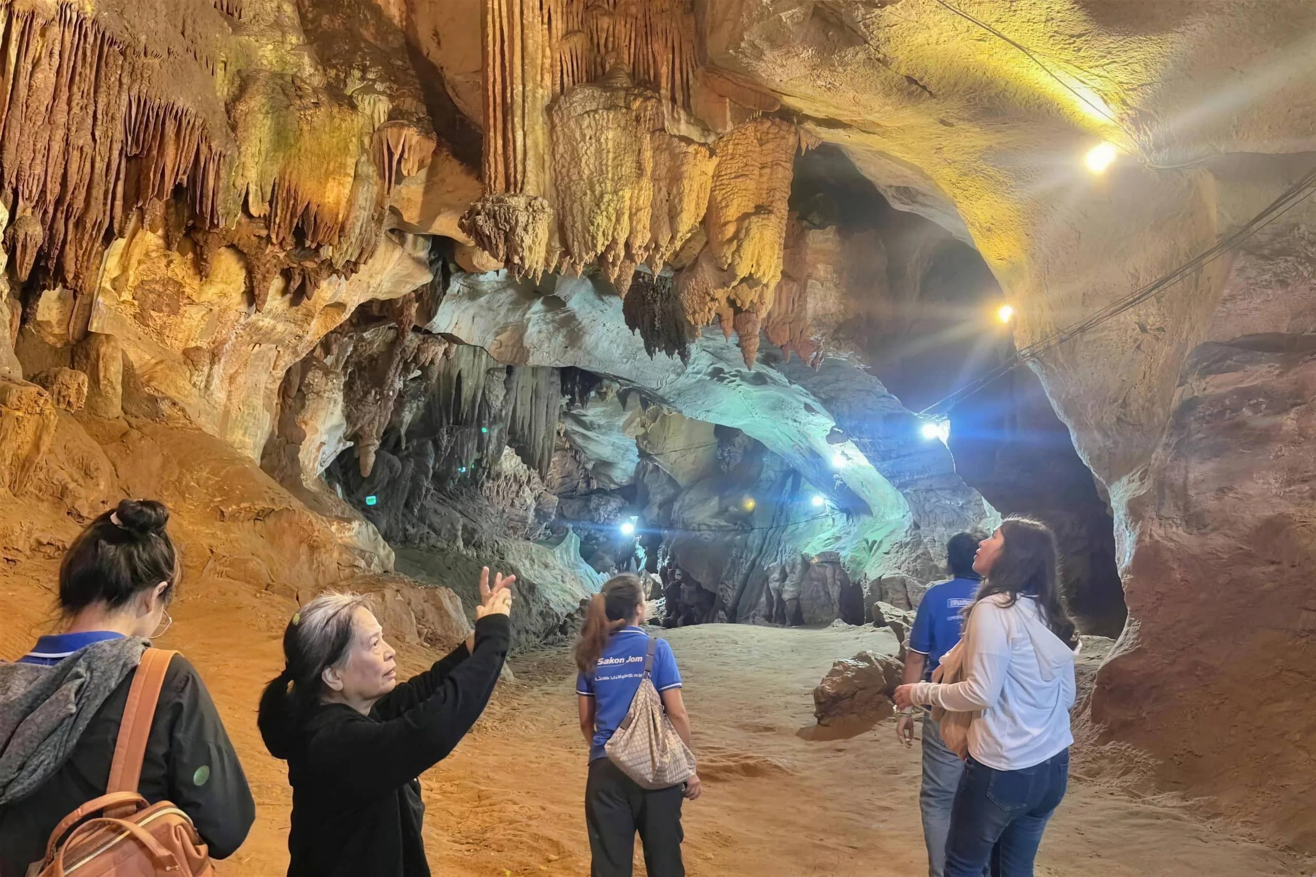 A guide points at lit rock formations as visitors look around inside Chiang Dao Cave
