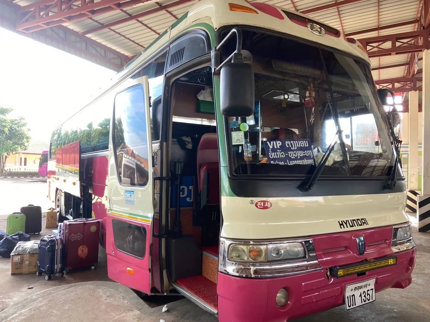 A pink and cream VIP bus waits under a station roof with luggage stacked beside it