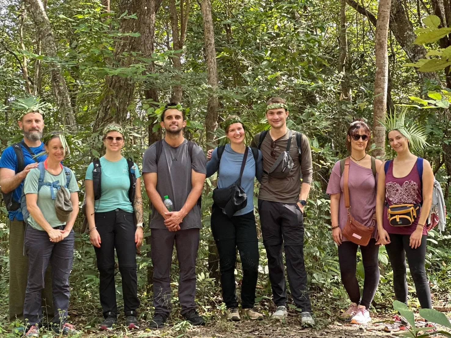 A group of trekkers wearing leaf crowns poses together on a forest trail at Doi Inthanon