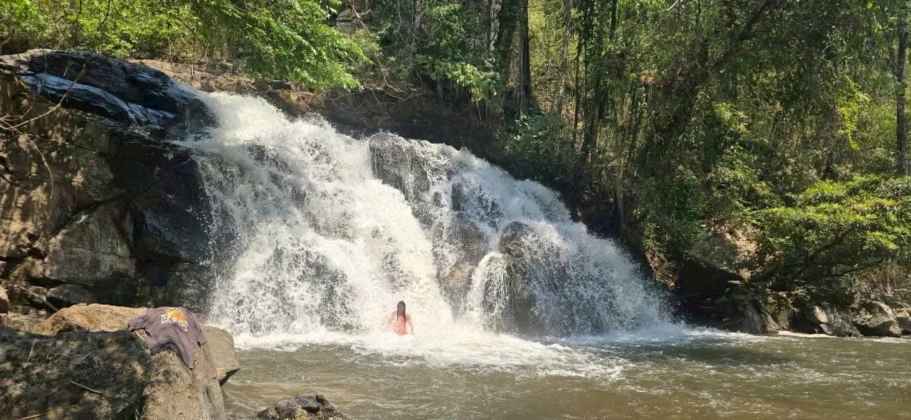 A swimmer bathes in the pool below a wide waterfall on the Doi Inthanon trek