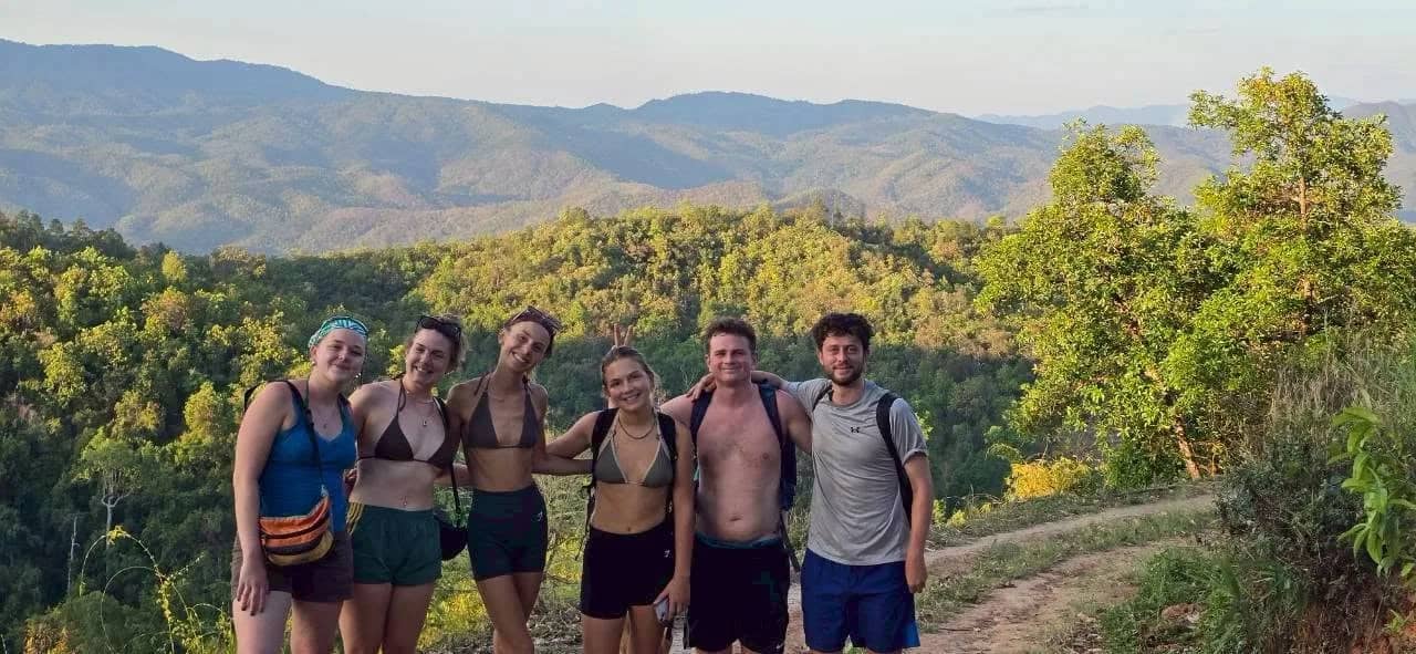 A group of trekkers poses on a ridge above forested valleys in the Doi Inthanon area