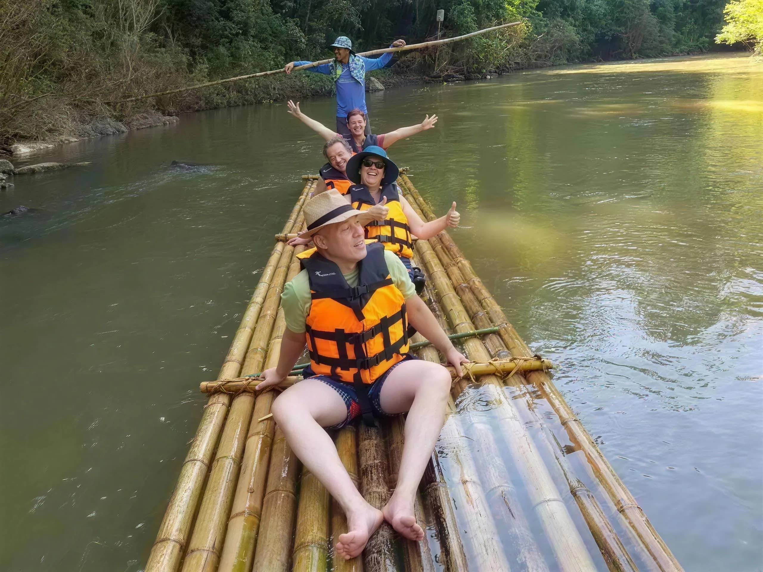 Smiling guests in life jackets ride a bamboo raft poled by a guide on the Mae Taeng River