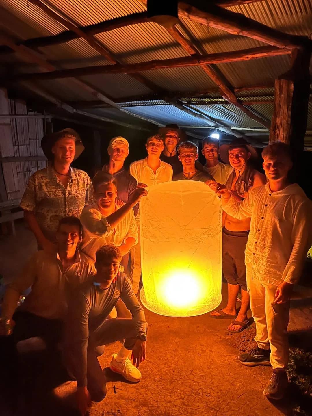 A group of trekkers gathers around a glowing paper lantern in a wooden hut at night