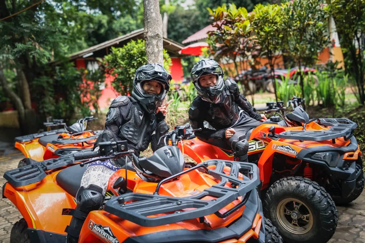 Two riders in helmets and protective jackets sit on orange ATV quad bikes before a ride
