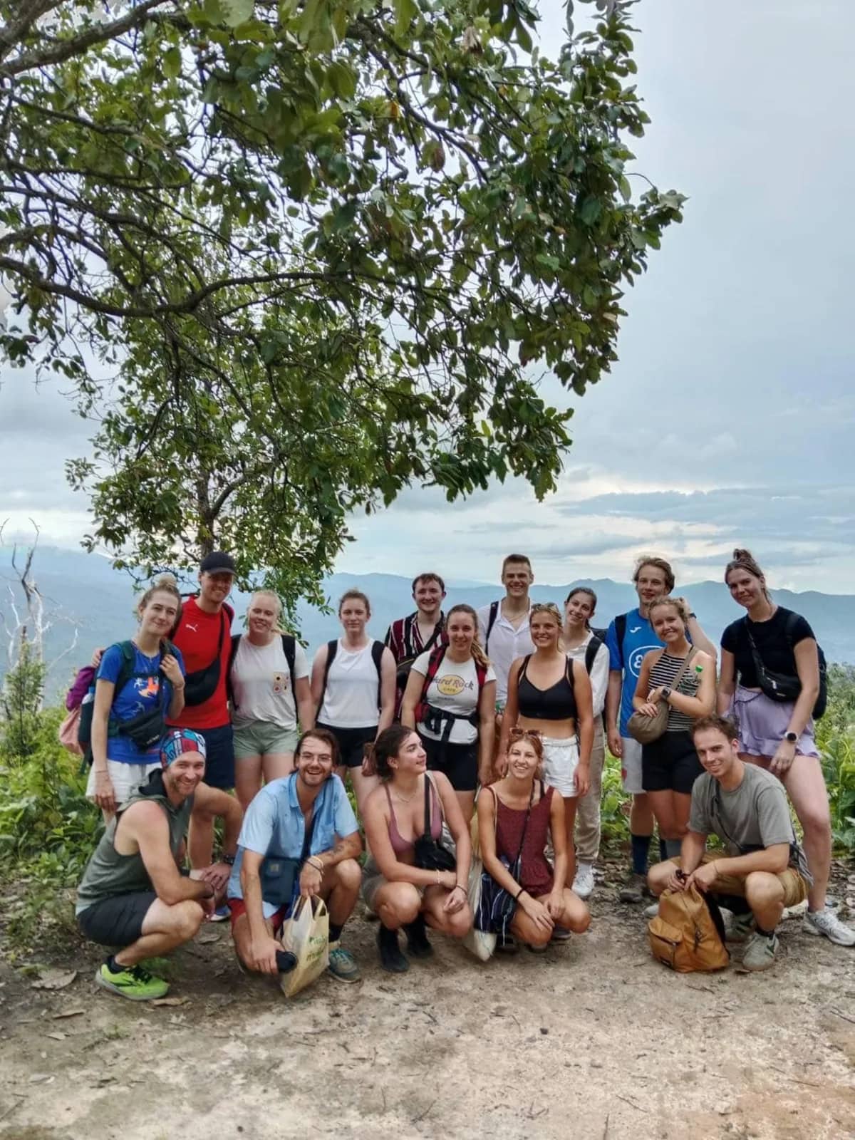 A large group of trekkers poses together at a hilltop viewpoint on a multi-day trek