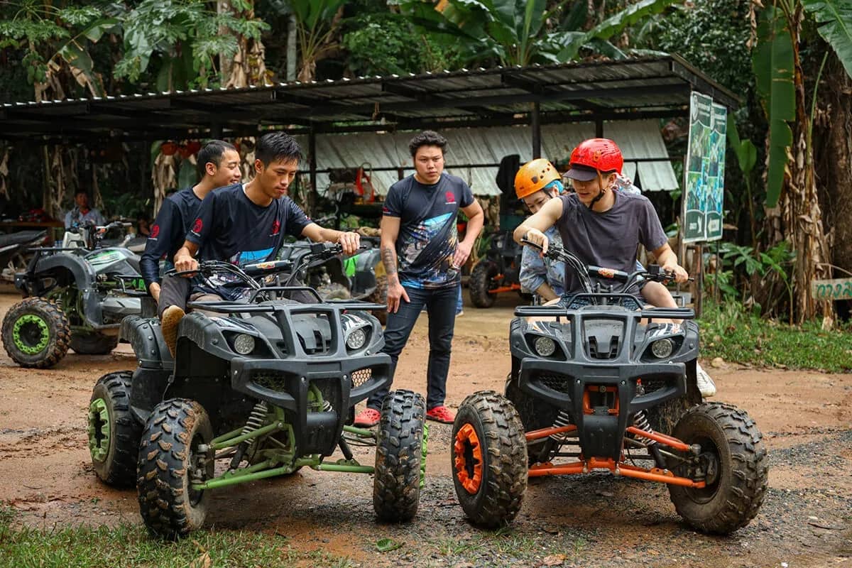 Riders in helmets climb onto ATVs as staff help them at a covered base camp