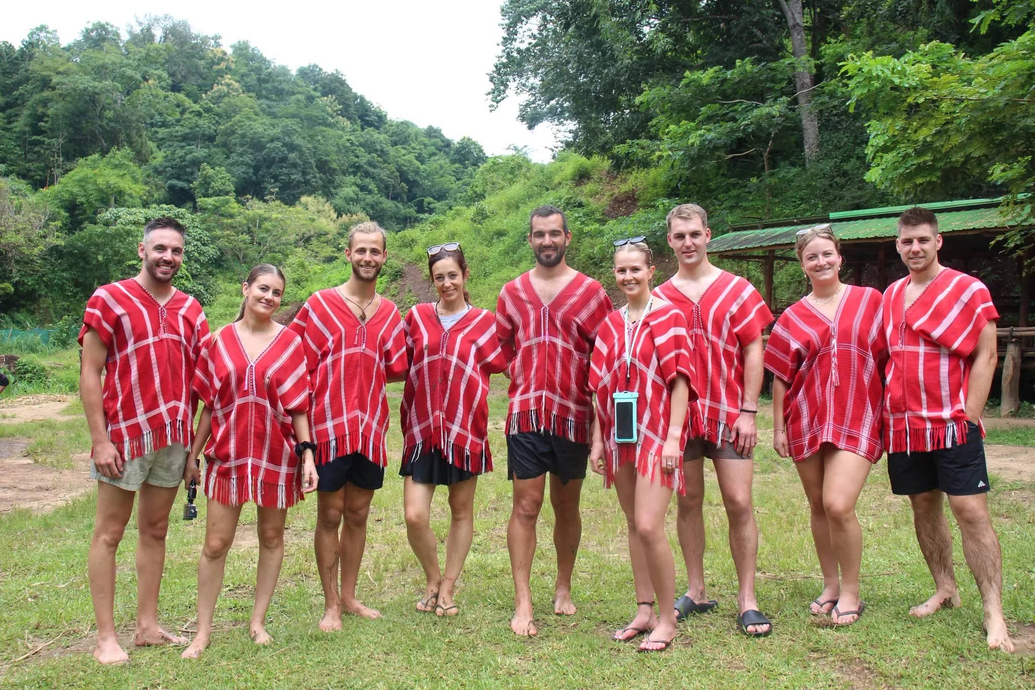 A group of visitors in matching red Karen shirts poses barefoot on the grass at the elephant camp