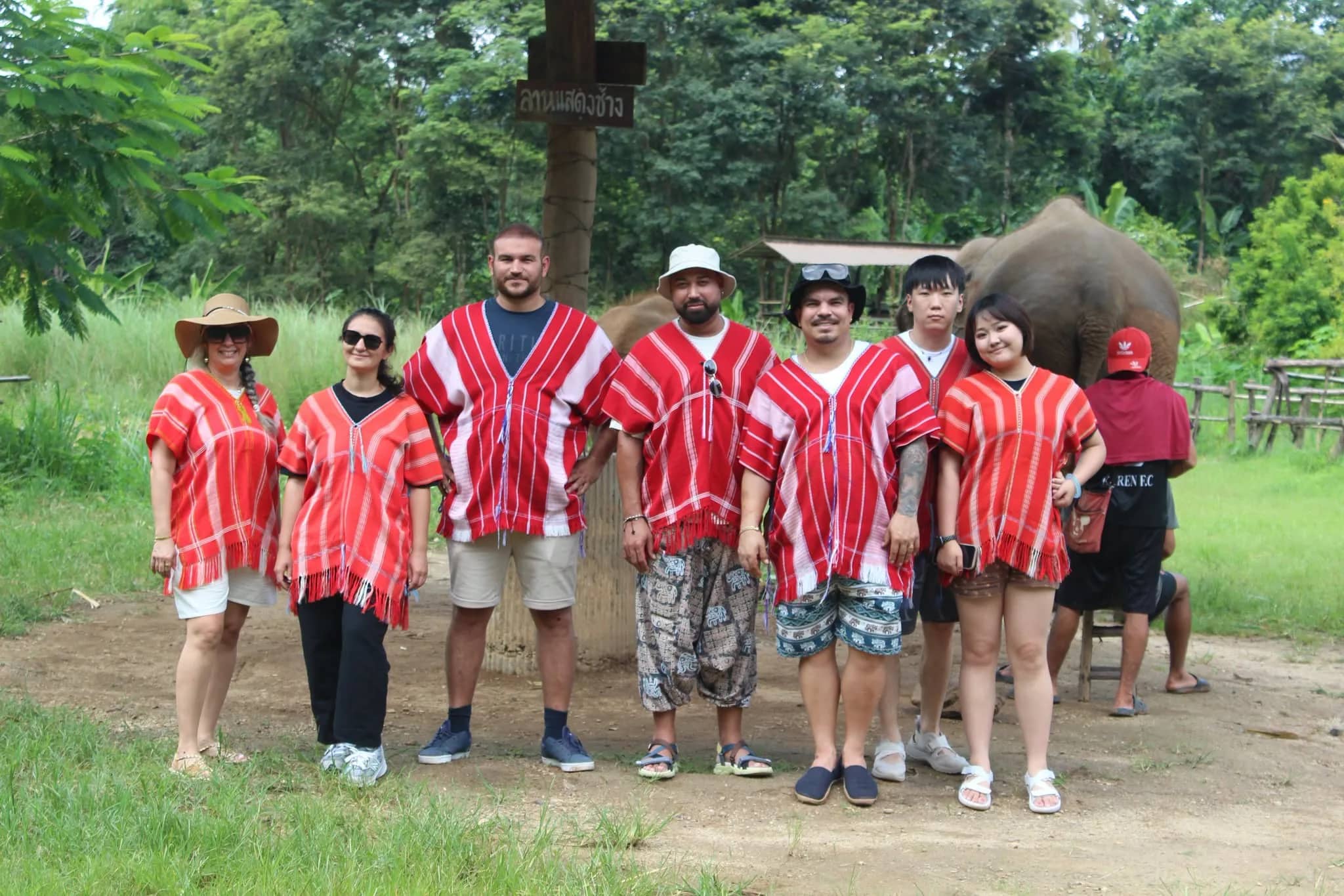 A group of visitors in red tunics poses together with an elephant behind them at the sanctuary