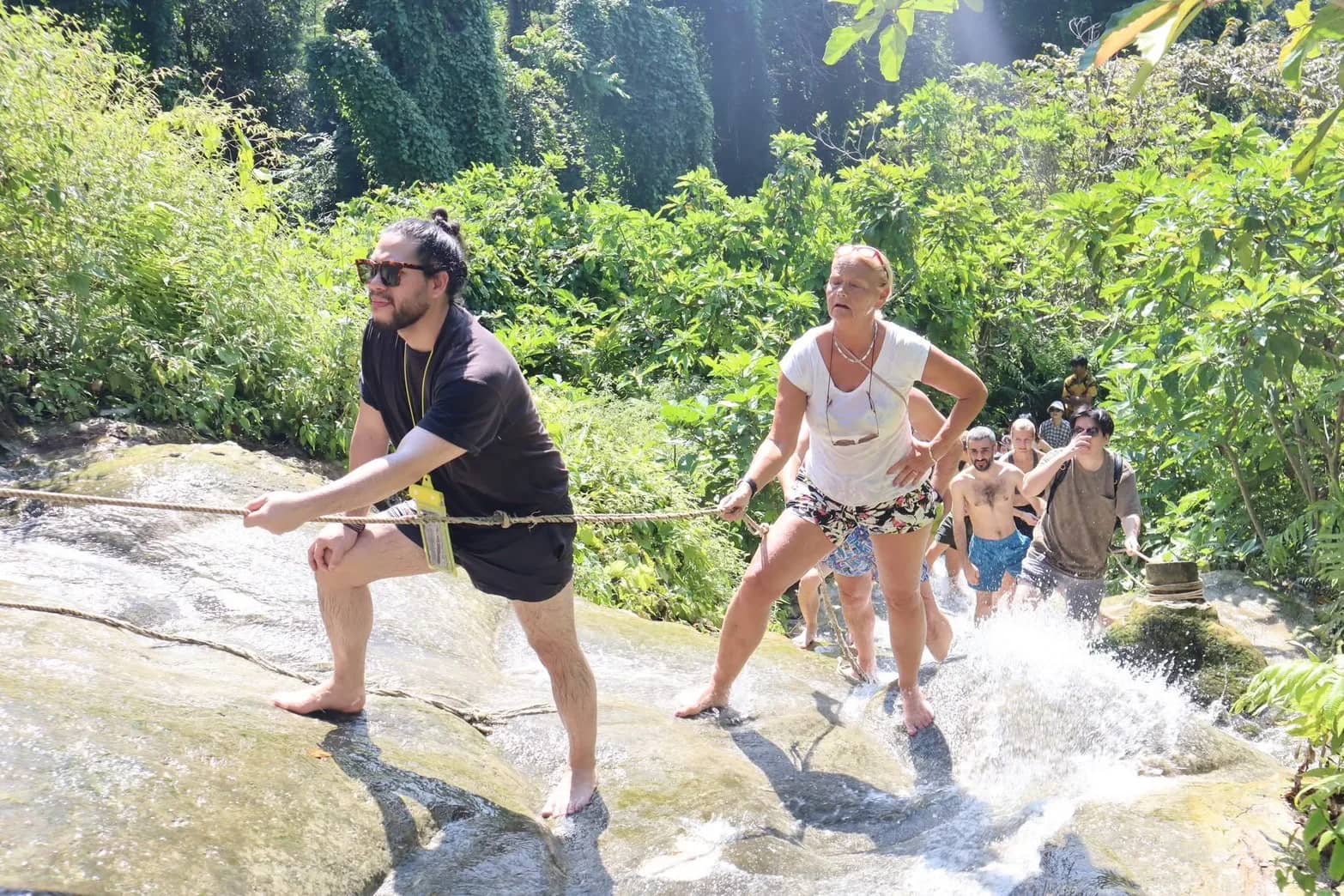 Visitors pull themselves up the rocks of the Sticky Waterfall using a rope as water flows past
