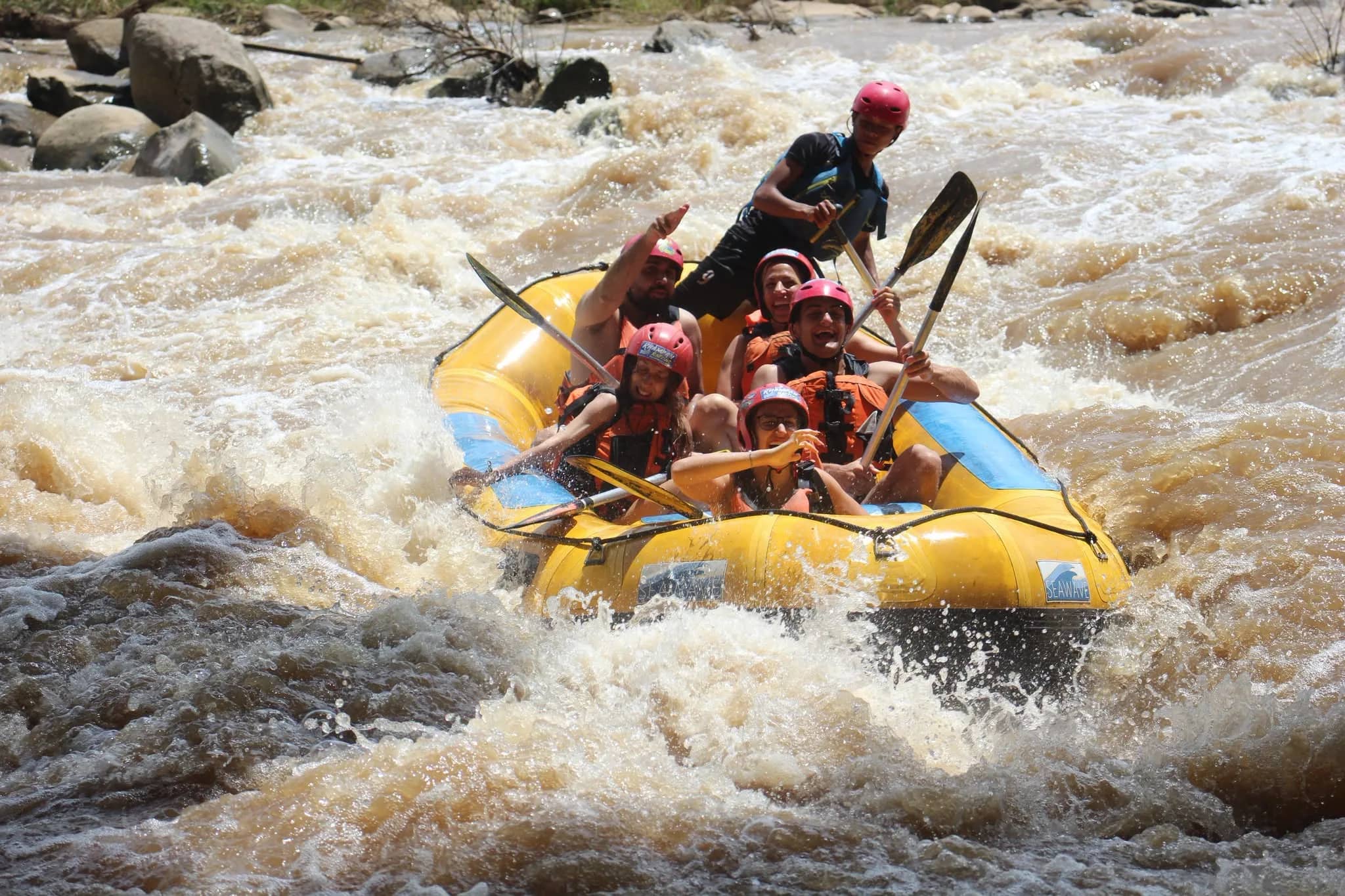 A yellow raft packed with helmeted paddlers plunges through churning whitewater rapids