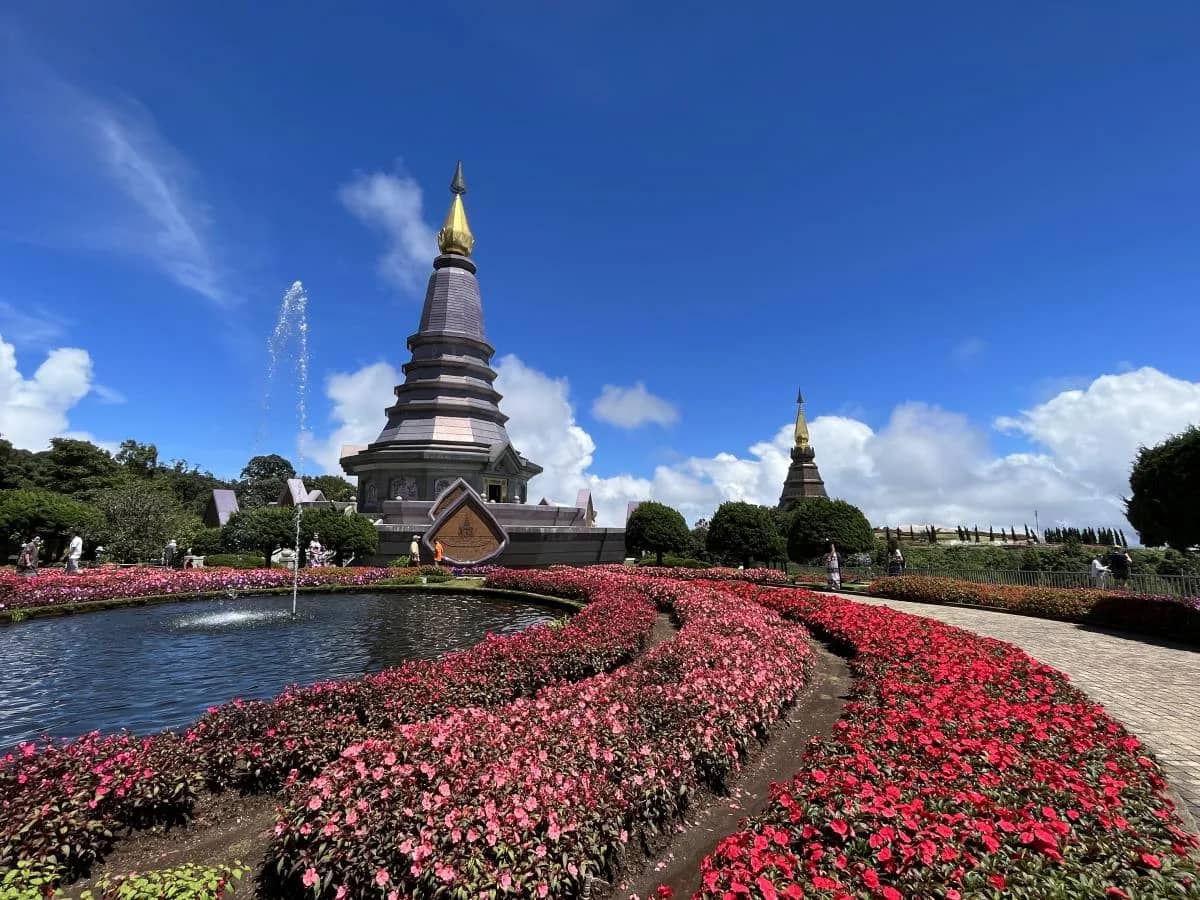 A pagoda rises above a fountain pond and red flower beds on a clear day at Doi Inthanon