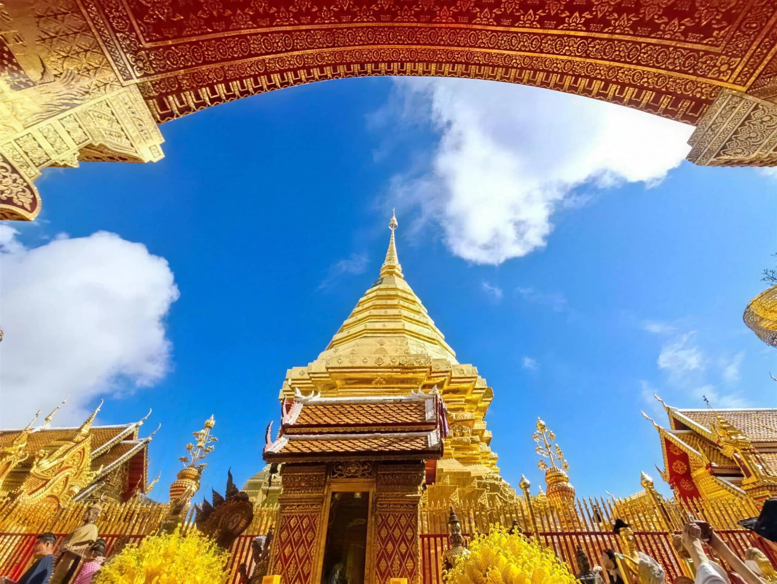 The golden chedi of Doi Suthep framed by a carved temple gateway against blue sky and clouds.
