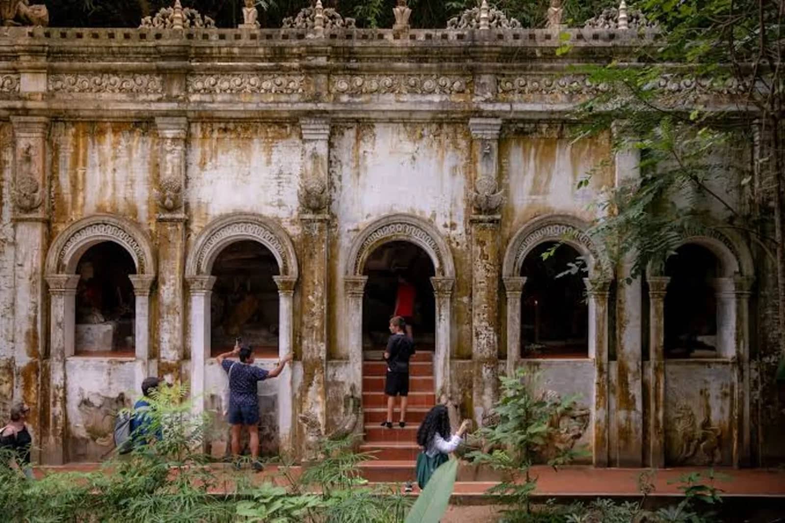 Visitors explore the moss-stained arched facade of an old temple building at Wat Pha Lat.
