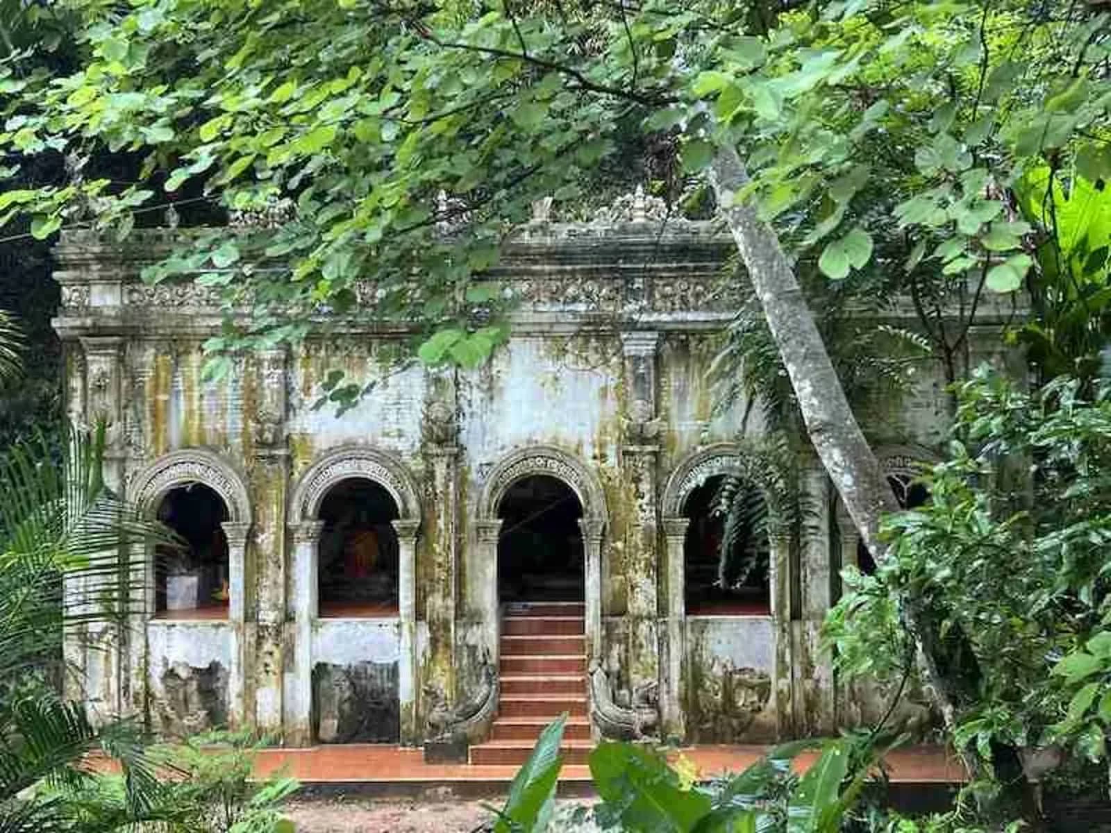 A weathered temple building with arched doorways sits among jungle trees at Wat Pha Lat.