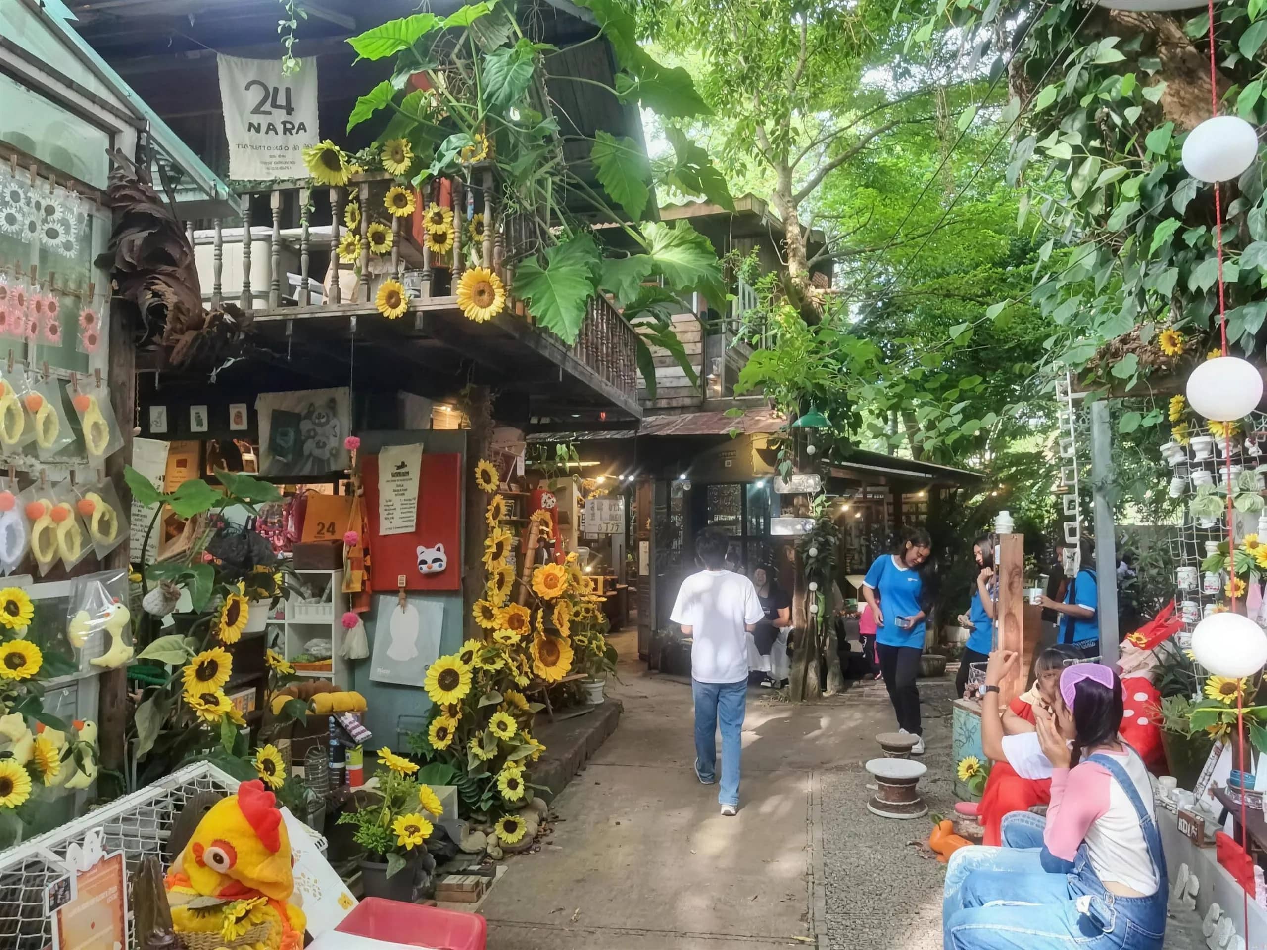 Visitors stroll a narrow lane of shops decorated with sunflowers and hanging lanterns