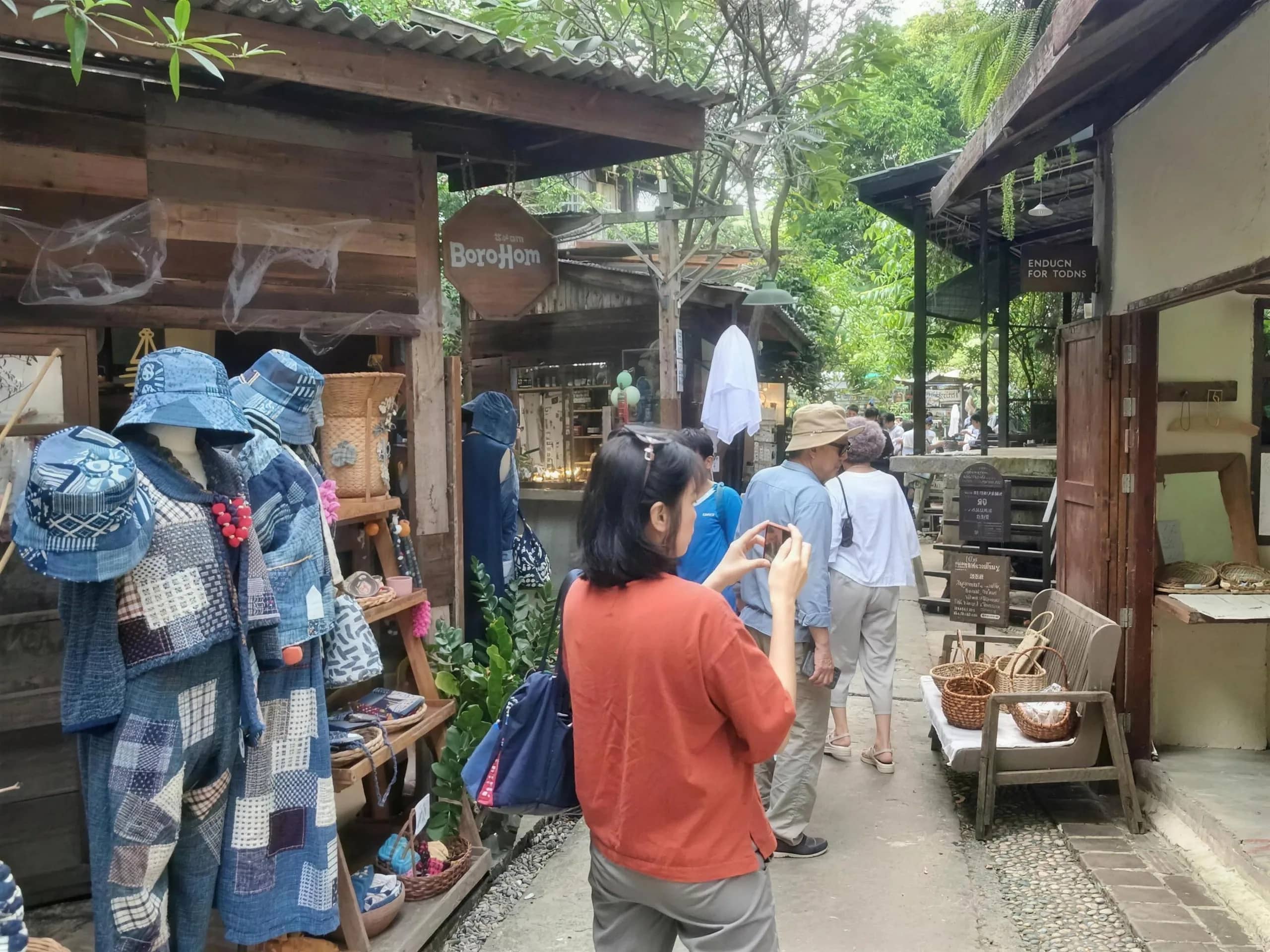 Visitors browse indigo clothing and wooden craft shops along a lane in Baan Kang Wat