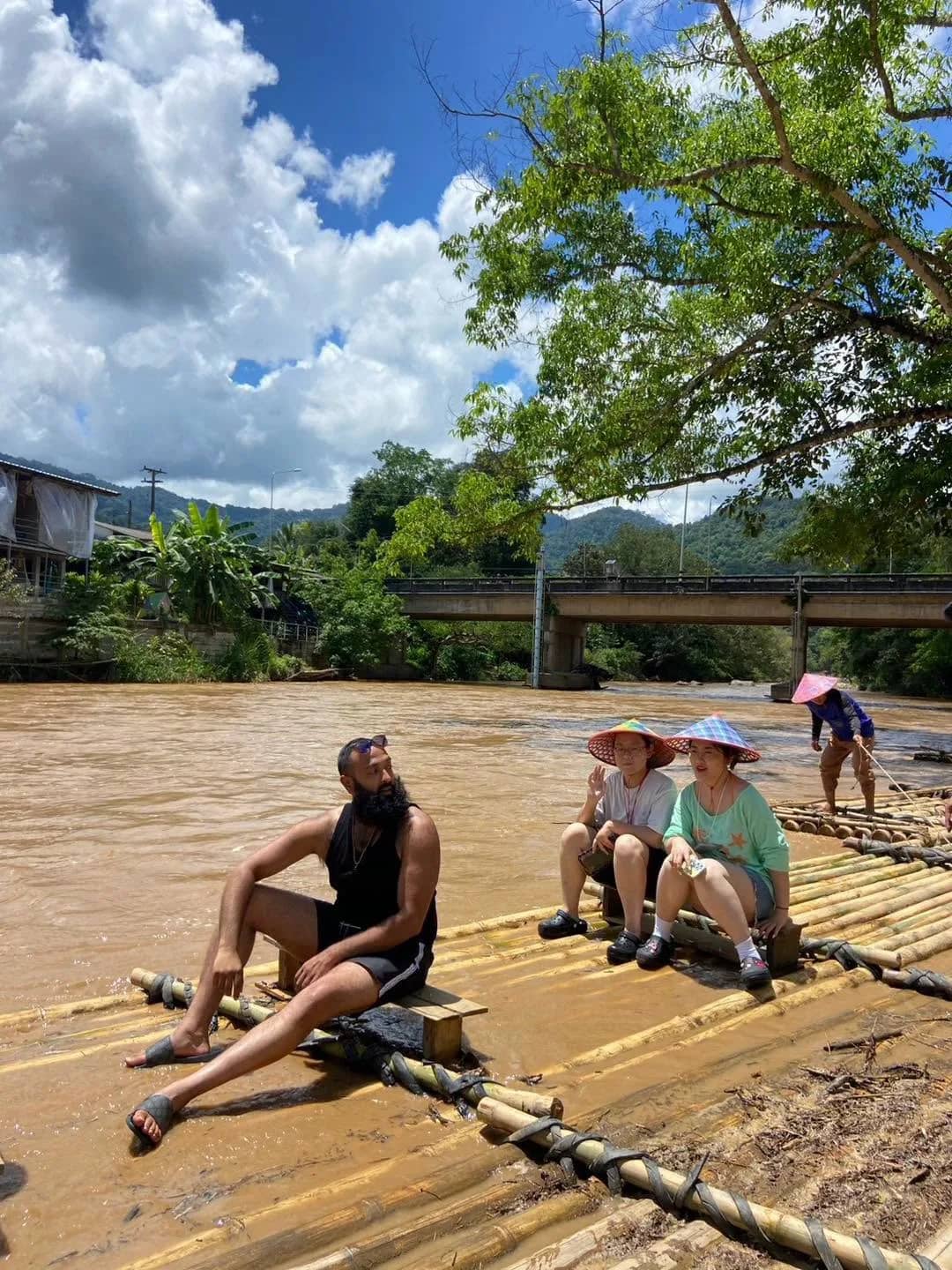Guests in sun hats sit on a bamboo raft floating down a wide river on a sunny day