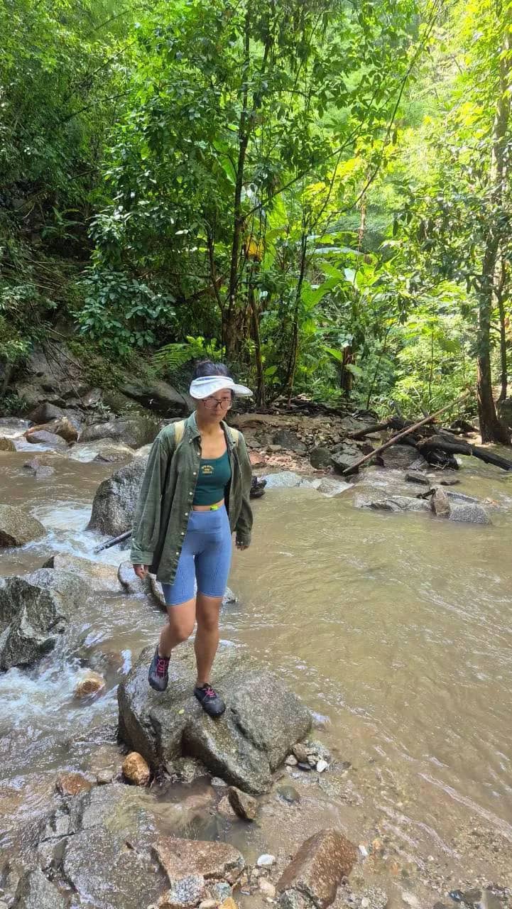 A hiker in a cap stands on rocks in a shallow forest stream on the way to a waterfall