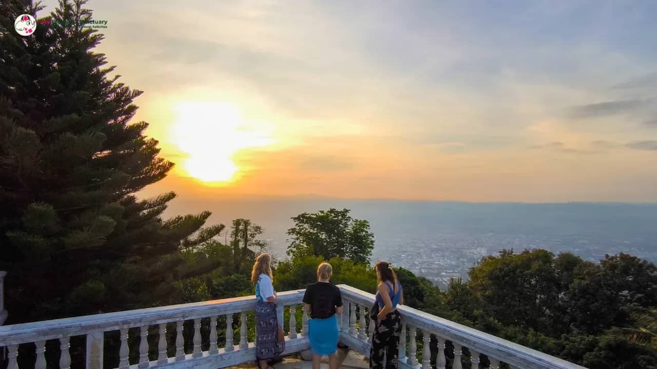 Three visitors at a white balustrade watch the sun rise over Chiang Mai from Doi Suthep