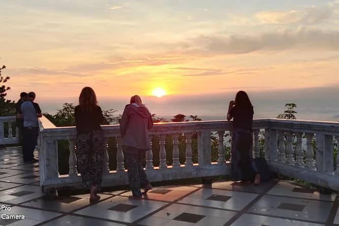 Visitors lean on a stone railing to watch the sun come up over the hazy plain below Doi Suthep