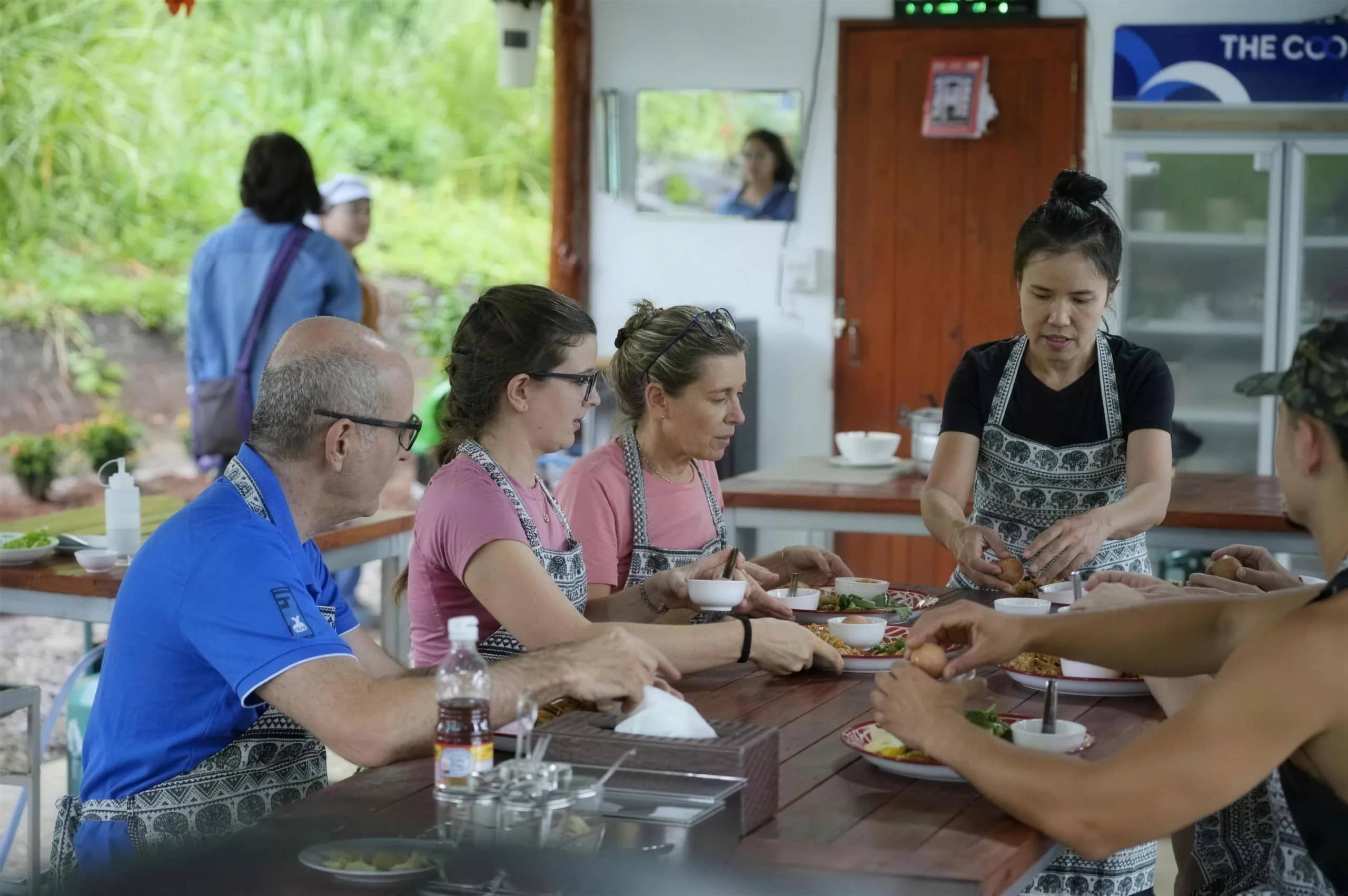Guests in aprons prepare ingredients together at a wooden table at the elephant sanctuary kitchen