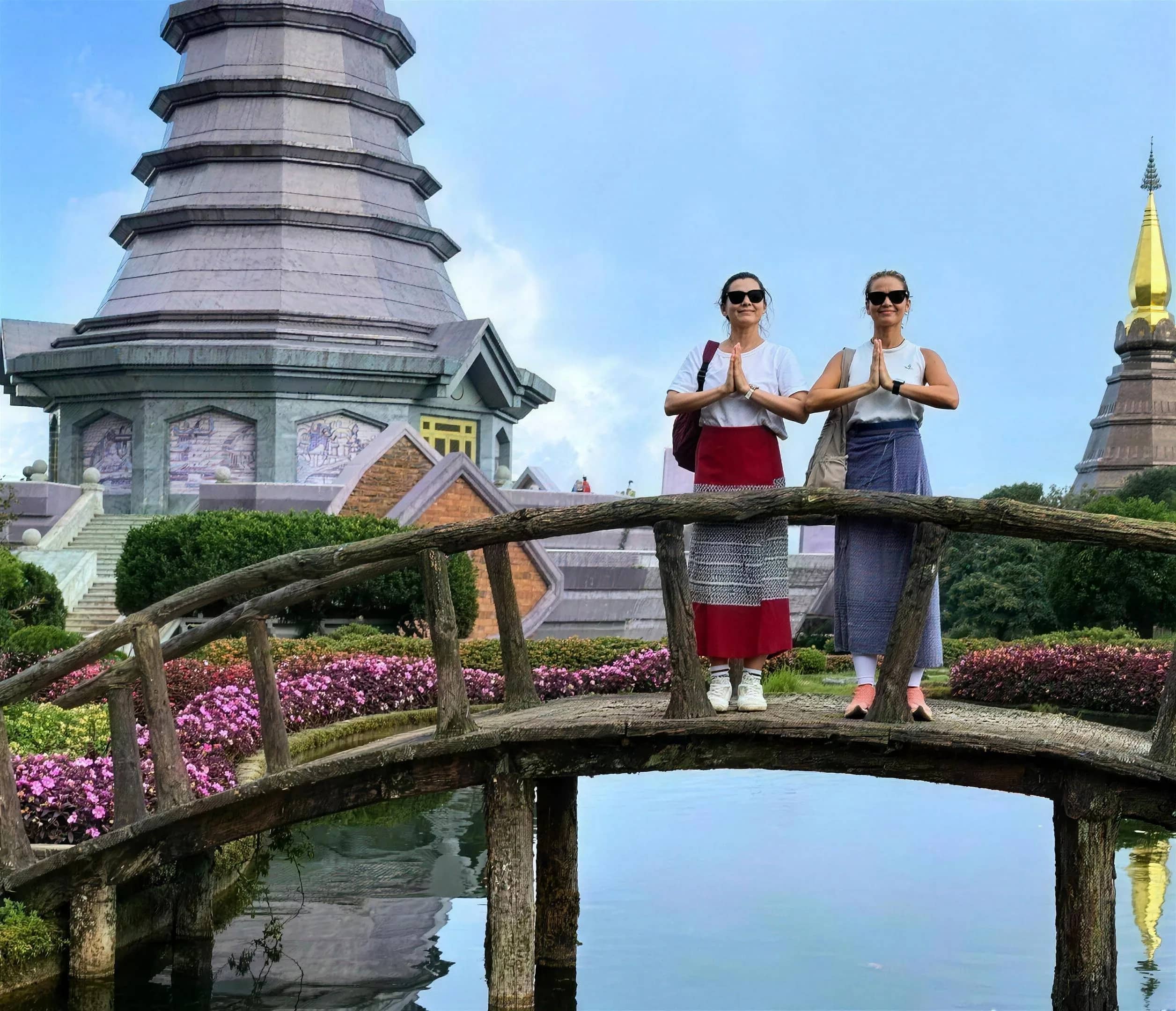 Two visitors greet with a wai on a garden bridge in front of the royal pagodas at Doi Inthanon