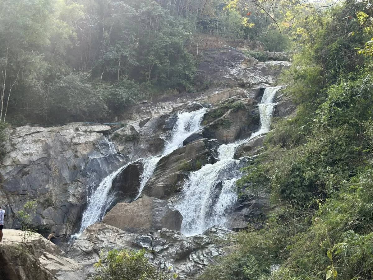 Water tumbles over a wide rocky cascade surrounded by forest on the elephant and waterfall tour