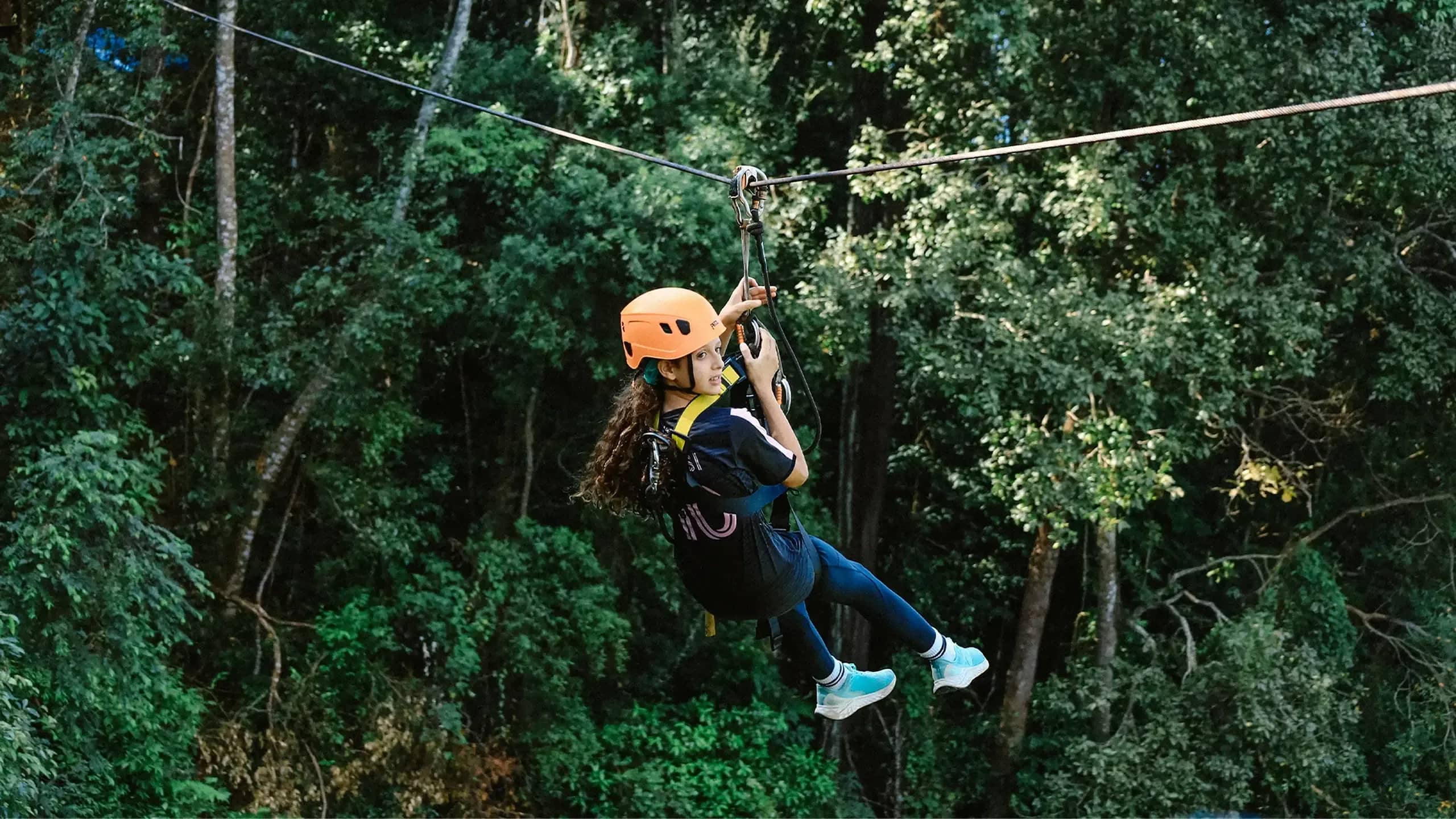A rider in an orange helmet glides along a zipline above dense green jungle at Flying Tiger Zipline