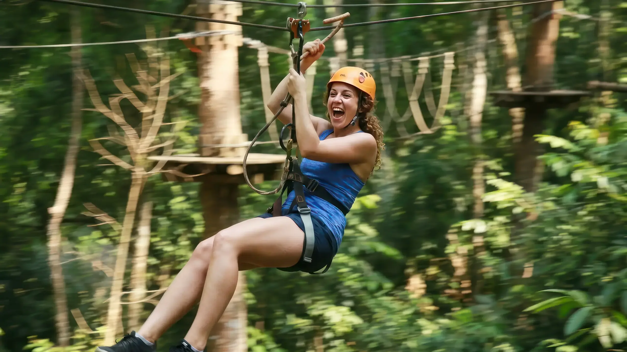 A smiling rider in a helmet and harness speeds along a zipline through the forest canopy