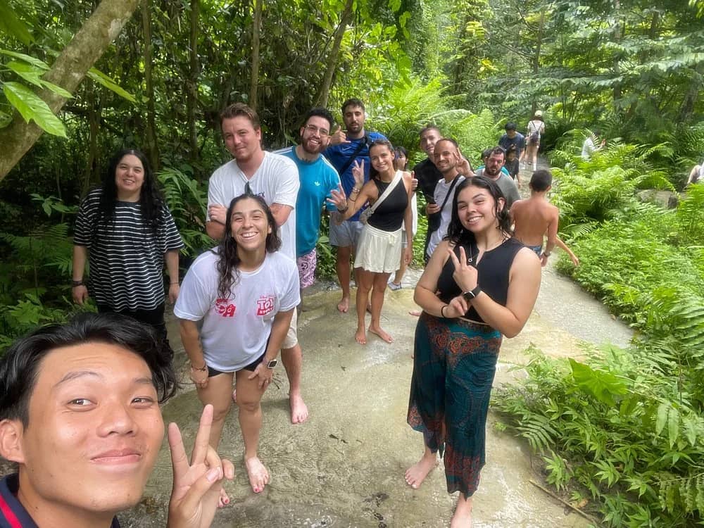 A smiling guide takes a selfie with a group of visitors on the rocks of the sticky waterfall.