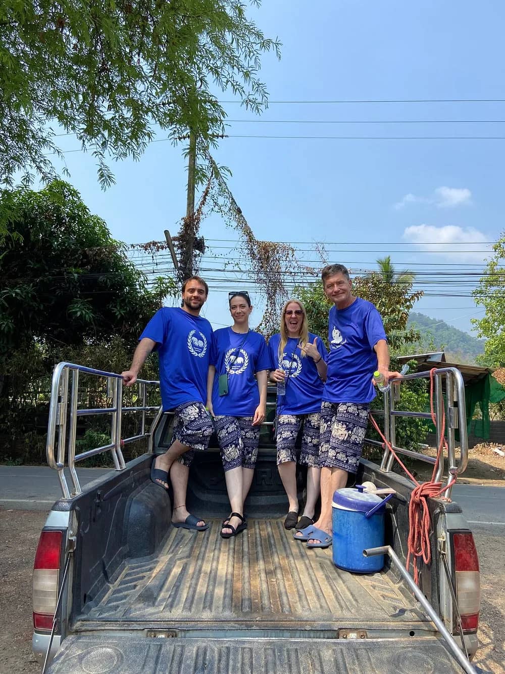 Four guests in matching blue shirts stand in the back of a pickup truck on a sunny day.