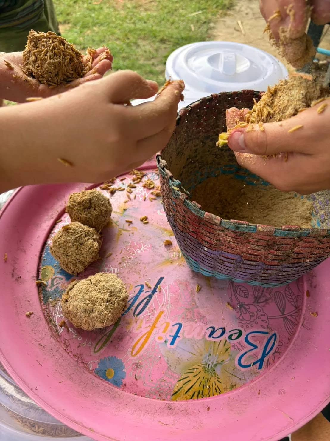 Hands roll food balls from a basket of mash onto a pink plate
