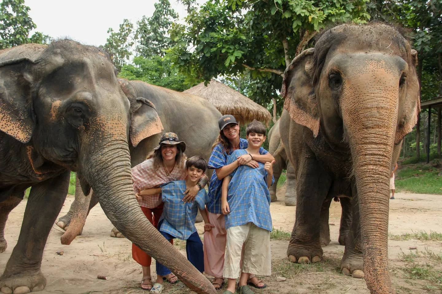 A family in blue cotton shirts poses between two elephants at a sanctuary near Chiang Mai