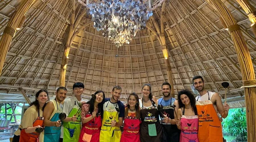 Cooking class guests in colourful aprons pose under the domed bamboo roof of Zabb E Lee Thai Cooking School