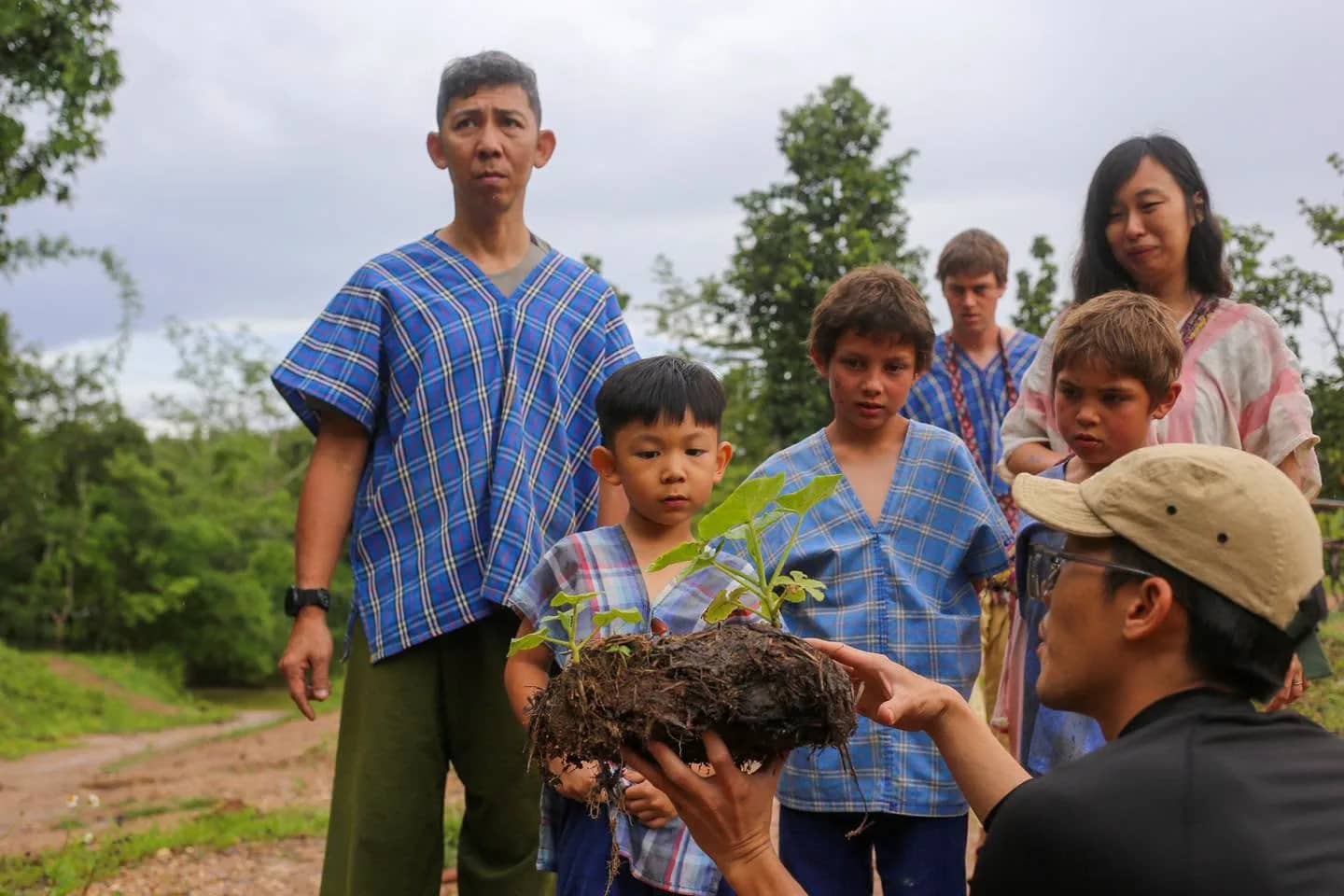 A guide shows a tree seedling with its soil to a group of children and adults in blue tops.