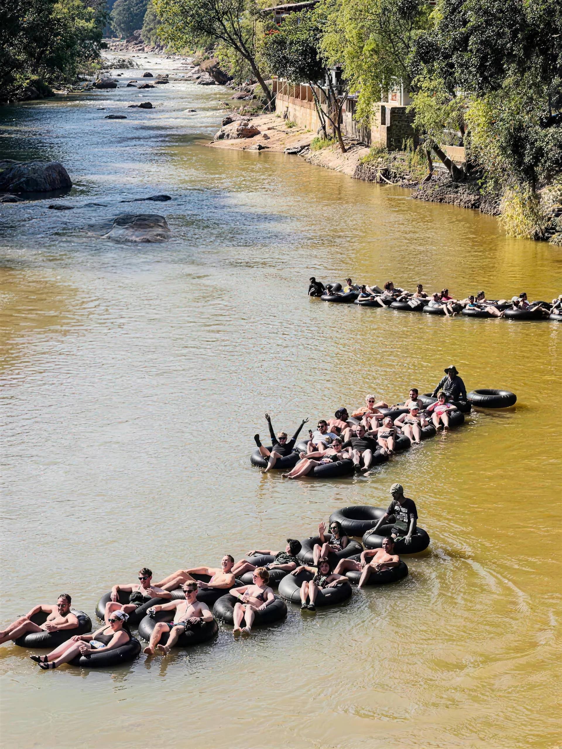 Three chains of linked rubber tubes carry groups of guests down a wide brown river.