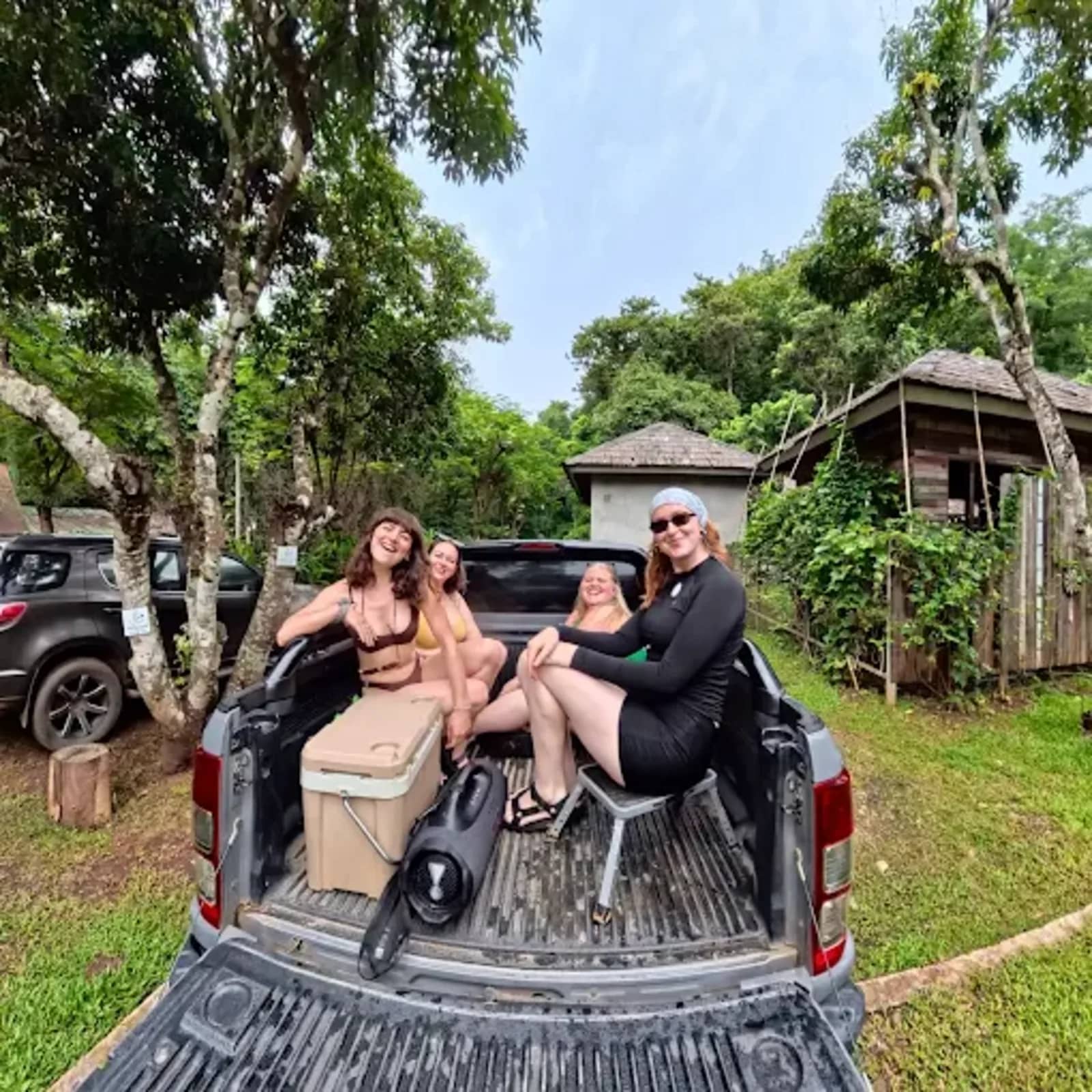 Smiling guests sit in the open back of a pickup truck with a cooler box before the tubing trip.