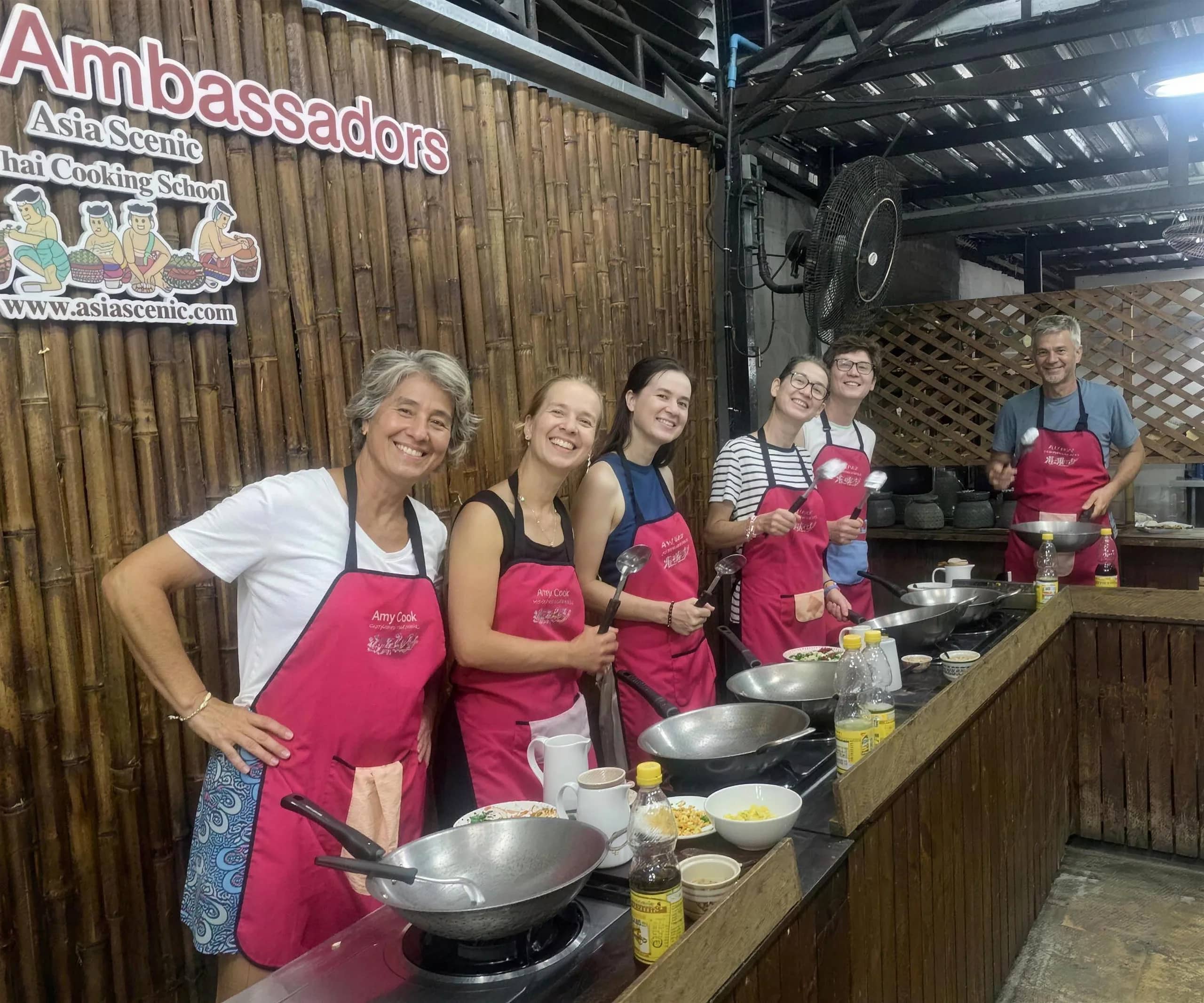 Smiling guests in pink aprons stand at their woks at Asia Scenic Thai Cooking School