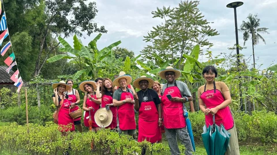 Guests in pink aprons and straw hats stand in the organic garden at Asia Scenic School